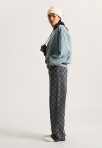 Lichtblauwe oversized sweatshirt, geruite grijze jeans en crèmekleurige geribbelde beanie. Getextureerde stof met zichtbare naden en zakken. Casual pasvorm.