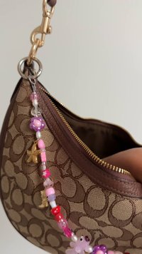 Brun mønstret håndtaske med lynlås, der har en dekorativ perlesnor med lyserøde og lilla detaljer samt en guldkant. Glat tekstur.