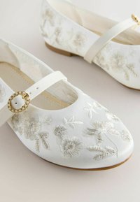 Balerini Mary Jane din satin alb, cu broderie florală și o cataramă accentuată cu perle. Vârf rotund, toc scăzut și curea ajustabilă pentru fixare.