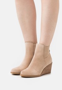 Bottines en suède beige avec un bout effilé et des panneaux latéraux en élastique côtelé, présentant un talon compensé à motifs.