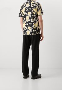 Camisa de manga corta con base negra, con un estampado floral en amarillo y blanco; combinada con pantalones negros y zapatos negros.