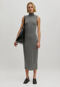 Graues ärmelloses Midikleid mit hohem Kragen, weichem Stoff und figurbetonendem Schnitt. Schwarze Tote-Bag und schwarze Blockabsatzschuhe.