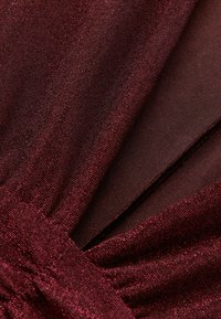 Burgundowa tkanina o błyszczącej, teksturowanej powierzchni z delikatnym połyskiem, zbierana w talii, warstwowa z kontrastowym, przezroczystym materiałem.