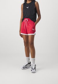 Top negro sin mangas y pantalones cortos rojos con ribete blanco, con un logo de Puma. Se lleva con calcetas blancas y zapatos deportivos negros. Tejido suave.