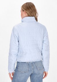 Giacca imbottita di colore azzurro, con cuciture orizzontali, colletto alto e polsini a coste, abbinata a jeans di denim a vita alta.