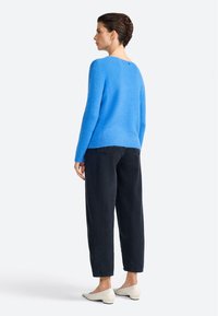 Maglione a maglia blu brillante con scollo rotondo, vestibilità rilassata, orlo a coste e maniche lunghe, abbinato a pantaloni neri larghi e scarpe beige.