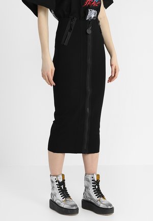 Svart midi kjol med frontdragkedja, strukturerad design och en slät textur. Matchad med metalliska silverfärgade ankelstövlar och svarta accenter.