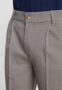 Brown and black houndstooth patterned trousers with a straight leg fit, featuring a single button closure at the waist.