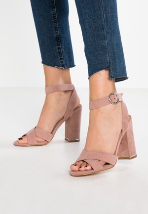 Vaaleanpunaiset mokkanahkaiset korkokantaiset sandaalit, joissa on neliömäinen kärki, nilkkaremmi ja tanakampi korko, jossa metallinen korostus. Yhdistetty lyhytlahkeisiin farkkuihin.