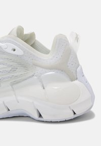 Vit sportskor med nätövre, tjock dämpad sula, dragöglor vid hälen och subtil logotyp på mittsålen och hälen.