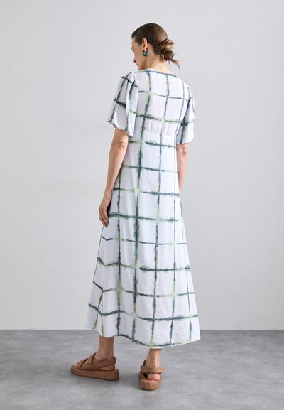 Witte midi-jurk met groen en zwart ruitpatroon, korte pofmouwen, relaxte pasvorm, gestructureerde stof, gecombineerd met bruine plateau-sandalen.