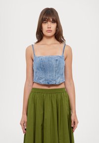 Top din denim, scurt, cu decolteu pătrat și bretele subțiri, având un design ajustat și detalii cusute, asortat cu o fustă verde cu talie înaltă.