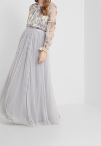 Longue jupe en tulle gris à pois, associée à un chemisier transparent à motifs floraux avec des manches bouffantes et des accents en dentelle aux poignets.