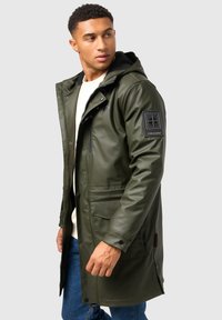 Green waterproof parka with a hood, featuring zippered and flap pockets, a textured patch on the sleeve, and a smooth, glossy finish.