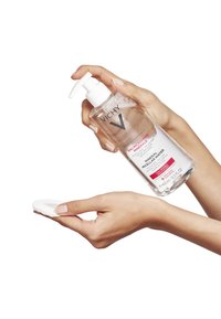 Vichy Mineral Micellar Water in a transparent bottle with a white pump, held above a hand with a cotton pad, featuring pink label text.