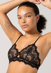 Bralette in pizzo nero con scollatura a V, motivo floreale intricato, spalline sottili regolabili e bordi a scallop.