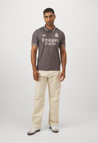 Grå, kortærmet polo-shirt med kontrastfarvet krave, der har hvide branding og elementer. Matchende med off-white, afslappede bukser og sneakers.