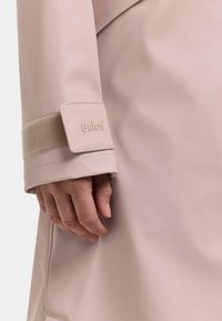 Hånd i lyserød vandtæt kåbeærme med justerbar rem mærket "Galon" på håndleddet.