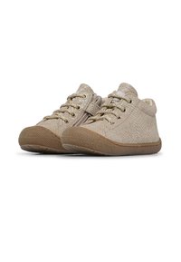 Zapatillas de deporte de un color beige claro con una superficie texturizada, punta redonda, ojetes metálicos para los cordones y suela de goma; diseñadas para la comodidad y la flexibilidad.