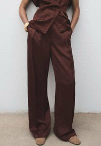 Pantaloni largi dintr-un material texturat de culoare burgundă, cu buzunare frontale, asortați cu un top corespunzător și o pereche de pantofi cu toc bej.