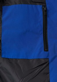 Niebieska łatka z tkaniny z czarnym zamkiem błyskawicznym na czarnym tle, ukazująca gładką teksturę i prostokątny kształt.