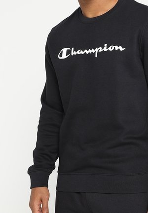 Sudadera negra con cuello redondo, hecha de una mezcla de algodón. Presenta un logo blanco de "Champion" en el pecho. Puños y dobladillo acanalados.