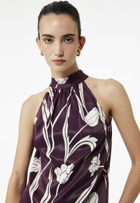 Ärmlös lila silketopp med vitt blommönster, med samlad halterneck och flödande design. Slät textur, minimalistisk stil.