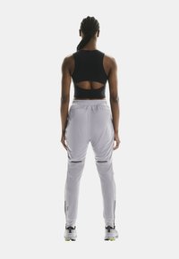 Top corto deportivo negro con espalda descubierta, combinado con pantalones jogger gris claro con cremalleras en los tobillos y cinturilla elástica. Zapatillas blancas.