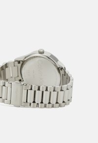 Stainless steel watch with a polished silver bracelet and round case. Knurled crown on the side and smooth back with engraved brand logo.