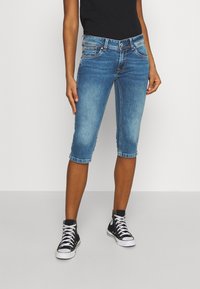 Shorts in denim di lunghezza al ginocchio di colore blu chiaro con finitura sbiadita, design a cinque tasche e chiusura frontale con bottone. Indossati con sneakers alte nere.