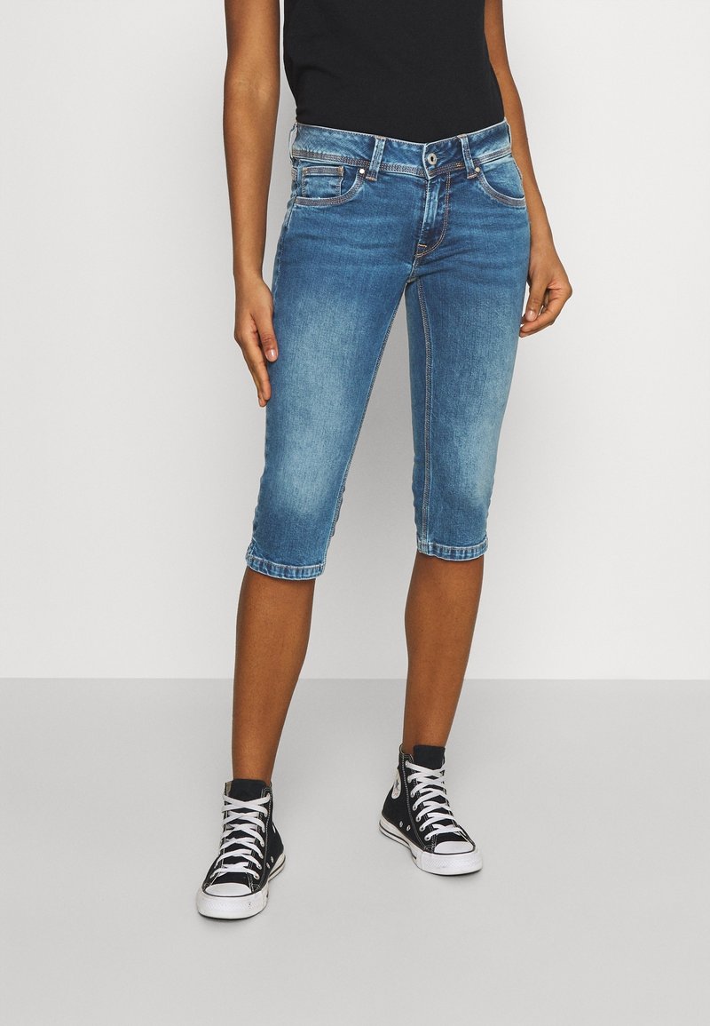 Shorts in denim di lunghezza al ginocchio di colore blu chiaro con finitura sbiadita, design a cinque tasche e chiusura frontale con bottone. Indossati con sneakers alte nere.