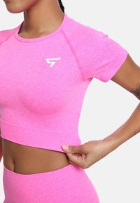 Kratka ružičasta atletska crop majica s okruglim izrezom i bijelim logotipom na prsima; izrađena od rastezljivog, teksturiranog materijala.