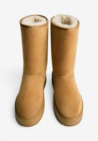 Stivaletti alla caviglia in suede beige con una morbida fodera interna pelosa. Punta arrotondata e suola piatta in gomma con dettagli di cucitura minima.