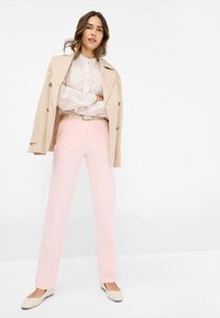 Lichtroze op maat gemaakte broek, gecombineerd met een beige trenchcoat en een bloempatronen blouse. Gladde stof met een slim fit ontwerp.