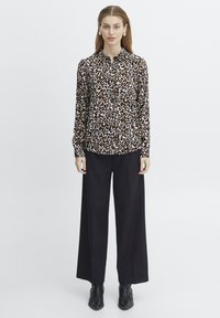 Camicia a fantasia leopardata con colletto, maniche lunghe e vestibilità morbida, abbinata a pantaloni neri a vita alta e gamba larga e stivaletti.