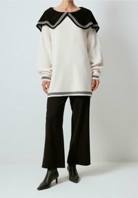 Pullover in Cremefarben mit übergroßem schwarzen Kragen und gestreiftem Saum. Gestylt mit schwarzen, weit geschnittenen Hosen und spitzen Stiefeletten. Glatte Textur.
