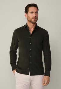 Camisa de botonadura en verde oscuro, hecha de una tela suave, con un cuello clásico, mangas largas y pequeños botones de contraste.