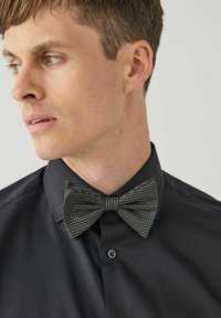 Czarna koszula z wywijanym kołnierzykiem, z szarym krawatem w muszkę o teksturowanym wzorze z małych białych kropek i eleganckim krojem.