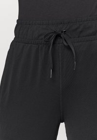 Schwarze Jogginghose aus glattem Material, mit einem elastischen Bund mit Kordelzug und einem Reißverschlussdetail vorne.