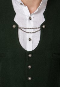 Dunkelgrüne Wollweste mit Rundhalsausschnitt, silbernen Knöpfen, dekorativen Kettenakzenten und einem weißen Hemd mit Kragen darunter.