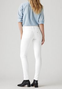 Jeans blancos ajustados con una textura suave, que cuentan con cinco bolsillos y un yugo trasero, combinados con una camisa de botones azul claro y botas de tobillo negras.