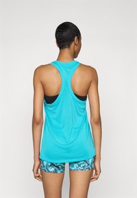 Turkis sportstop med racerback-design; letvægtsstof; parret med mønstrede blå og sorte shorts; glat tekstur.