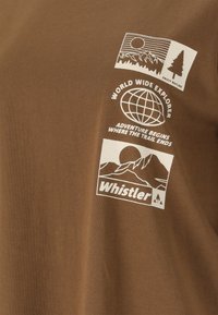 Brauner Stoff mit weißen, outdoor-inspirierten Grafiken, darunter Berge, eine Weltkugel, ein Baum sowie die Schriftzüge "World Wide Explorer" und "Whistler".