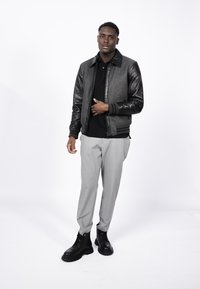 Men's bomber jacket in grey wool blend with black leather sleeves; worn over a black shirt with light grey trousers and black lace-up boots.