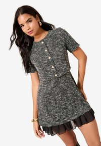 Lühikeste varrukatega mustvalge tuletikuga kleit ümmarguse kaelusega, kuldsete nööpidega ja kihilise õhukese volangiga äärega.