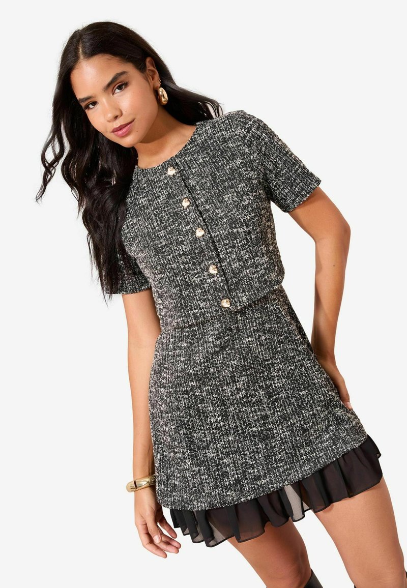 Lühikeste varrukatega mustvalge tuletikuga kleit ümmarguse kaelusega, kuldsete nööpidega ja kihilise õhukese volangiga äärega.