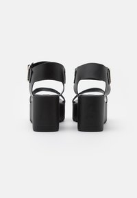 Sandalias de tacón alto negras con un amplio tacón de bloque, correa ajustable con hebilla y diseño de parte trasera abierta, con textura de cuero suave.