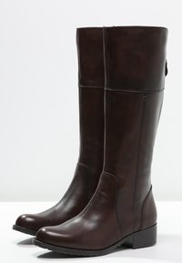 Bottes montantes en cuir marron avec une texture lisse, bout rond, talon léger et détail de fermeture éclair latérale. Design minimaliste, sans motifs visibles.
