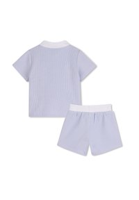 Ανοιχτόμπλε πλεκτό πόλο με κοντά μανίκια και λευκό γιακά, συνδυασμένο με σορτς με ελαστική μέση στο ίδιο χρώμα. Μαλακή υφή, casual σχεδίαση.