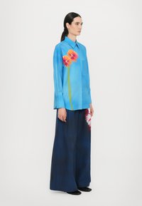 Blue shirt with orange and pink floral print, long sleeves, and a chest pocket; paired with wide-leg dark pants, smooth texture.